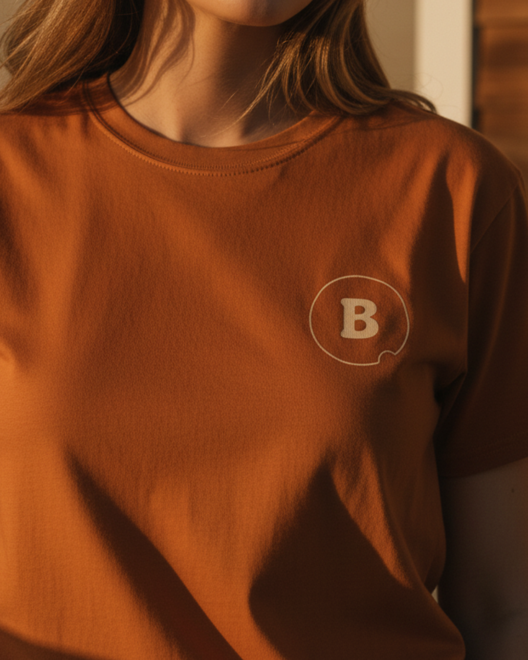 Brown t-shirt with a logo featuring the letter 'B' on a blurred background